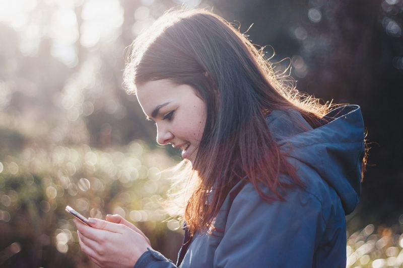 Adolescente olhando o celular ao ar livre, à luz do fim da tarde